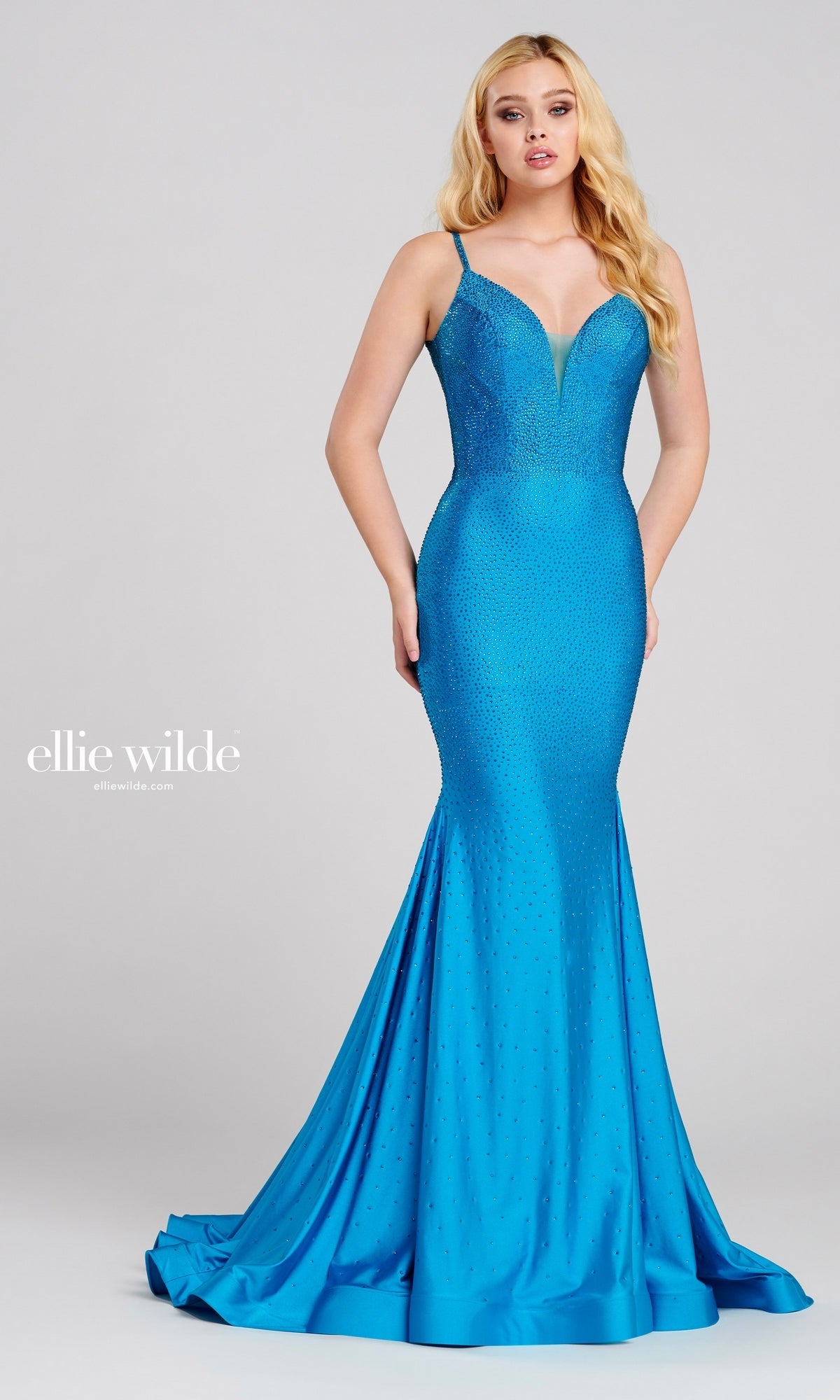 A woman wears the Ellie Wilde Beaded Mermaid Prom Dress with Cut Out—a fitted, sleeveless blue gown featuring subtle embellishments—while standing against a plain background.